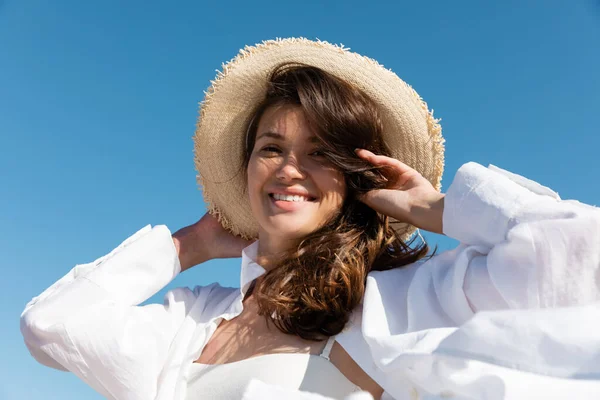 水着姿の幸せな若い女性と青い空に向かって麦藁帽子をかぶった白いシャツの低角度ビュー — ストック写真