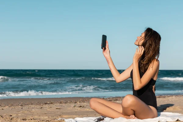 Jovem Morena Maiô Tomando Selfie Enquanto Sentado Cobertor Perto Mar — Fotografia de Stock