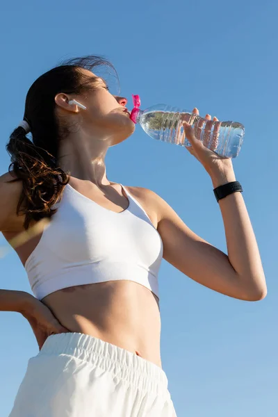 青い空に対するワイヤレスイヤホン飲料水の若い女性の低角度ビュー — ストック写真