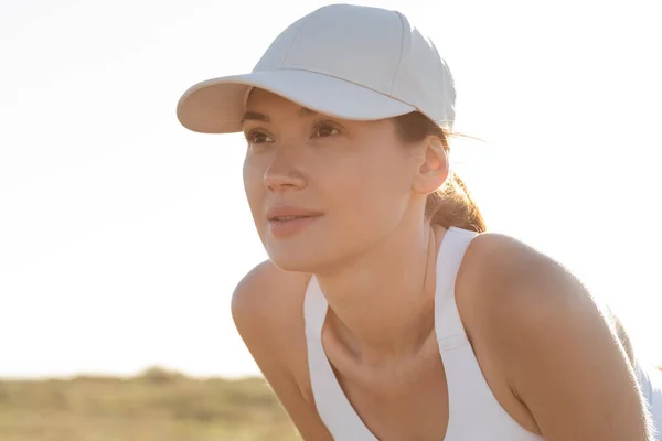 Beyzbol şapkalı ve spor sutyenli esmer bir kadın başka tarafa bakıyor. 