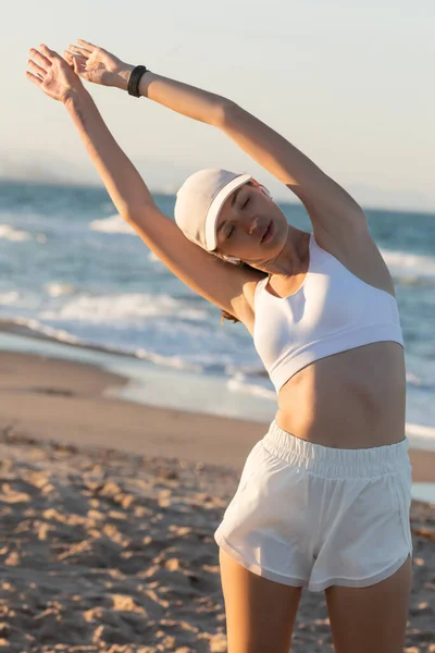 Beyzbol şapkalı ve deniz kenarında kablosuz kulaklıklı genç bir kadın. 