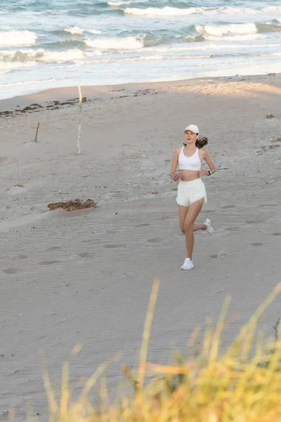 Young Sportive Woman Baseball Cap Wireless Earphone Running Sand Sea — Stock Photo, Image