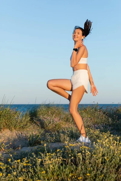 幸せなフィット女性でスポーツショートパンツと無線イヤフォンジャンプ近く青い海 — ストック写真