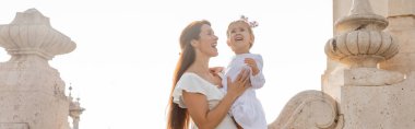 Brunette woman holding kid near stone Puente Del Mar bridge in Valencia, banner 