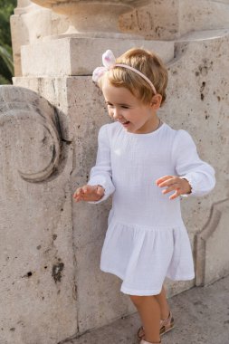 Smiling toddler girl in summer dress walking near stone Puente Del Mar bridge in Valencia