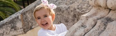 Happy toddler girl looking at camera near stone Puente Del Mar bridge in Valencia, banner 
