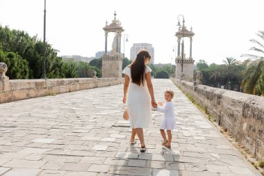 Woman holding hand of child in dress while walking on Puente Del Mar bridge in Valencia