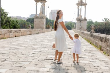 Positive woman in dress holding hand of baby on Puente Del Mar bridge in Valencia