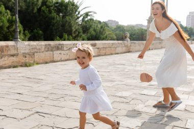 Happy child running near blurred mom on Puente Del Mar bridge in Valencia