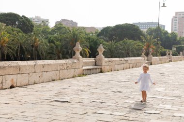 Smiling toddler girl in white summer dress walking on Puente Del Mar bridge in Valencia