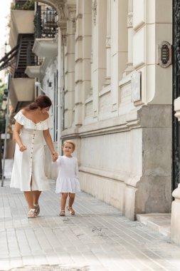 Woman and child holding hands while walking on urban street in Valencia