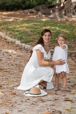 Kid pointing with finger near mom and straw hat in park in Valencia
