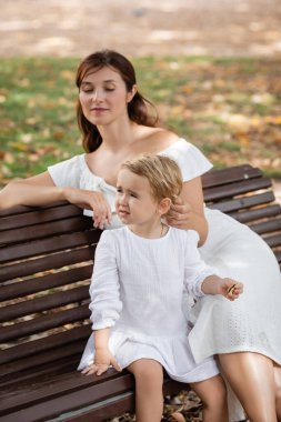 Toddler girl holding cookie near mom on bench in park 