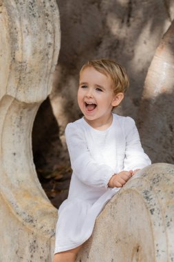 İspanya 'da parktaki taş bankta oturan, beyaz elbiseli, heyecanlı çocuk. 