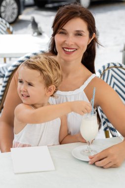 Gülümseyen anne, İspanya 'da açık hava kafesinde elinde milkshake ile çocuğun yanındaki kameraya bakıyor. 