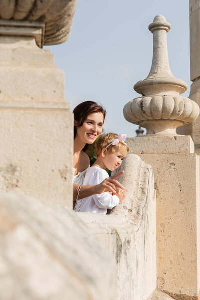 Smiling mother pointing with finger near daughter on stone Puente Del Mar bridge in Valencia