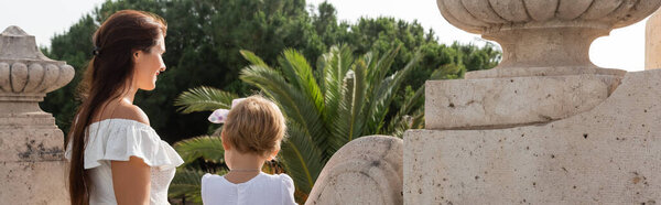 Smiling woman looking away near daughter on stone Puente Del Mar bridge in Valencia, banner 