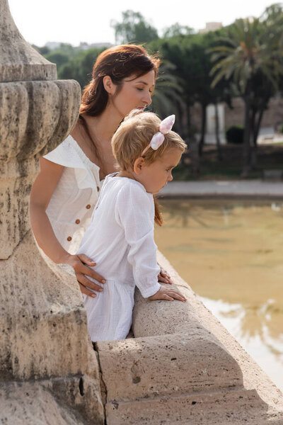 Side view of woman touching baby daughter on Puente Del Mar bridge above river in Valencia