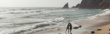 bearded man hugging girlfriend in dress while walking in ocean water, banner clipart