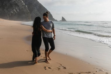 Mutlu adam, kız arkadaşıyla okyanus kenarında ıslak kumda dans ediyor.