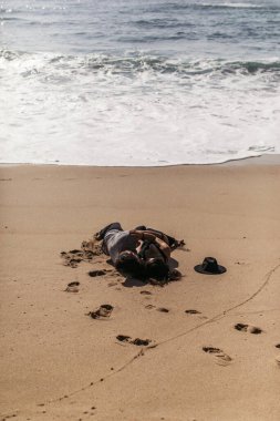 Çiftler kumsalda okyanus kenarında ıslak kumda sarılıp yatıyorlar. 