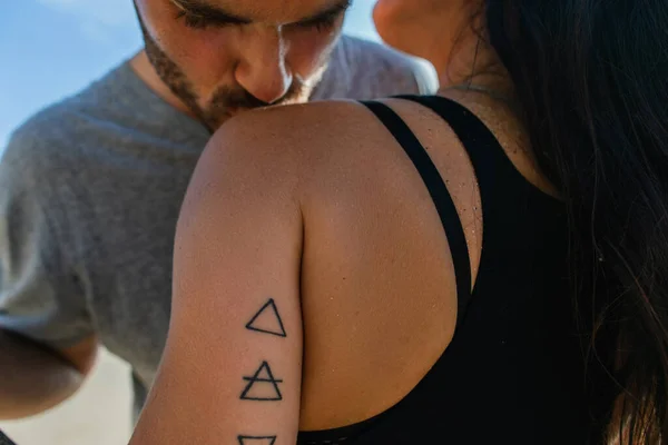 Sakallı adam dövmeli esmer kız arkadaşının omzunu öpüyor. 