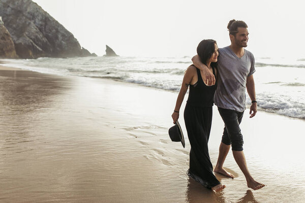 happy man in t-shirt walking with girlfriend on wet sand near ocean