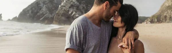 Neşeli sakallı adam ve neşeli kadın okyanus kenarında el ele tutuşuyorlar.