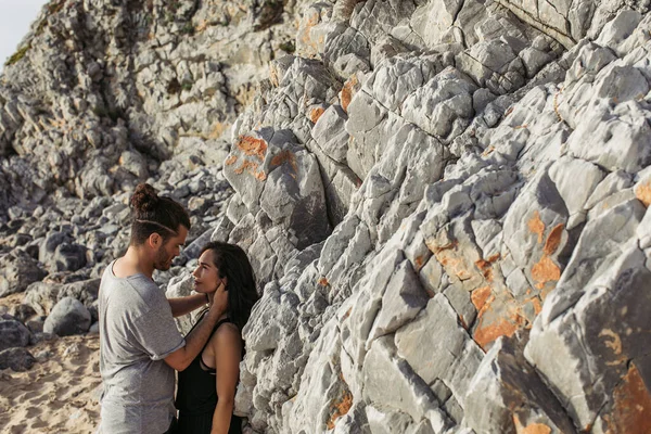 髭を生やした男がビーチの岩の近くにいる彼女を抱きかかえて見て — ストック写真