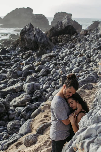 Uomo Barbuto Abbracciare Fidanzata Mentre Piedi Vicino Rocce Sulla Spiaggia — Foto Stock
