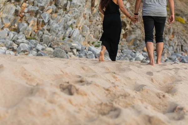 夫妻手牵着手在岩石附近的沙滩上散步的剪影 — 图库照片