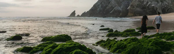 Vista Trasera Pareja Caminando Cerca Piedras Musgosas Verdes Océano Durante —  Fotos de Stock