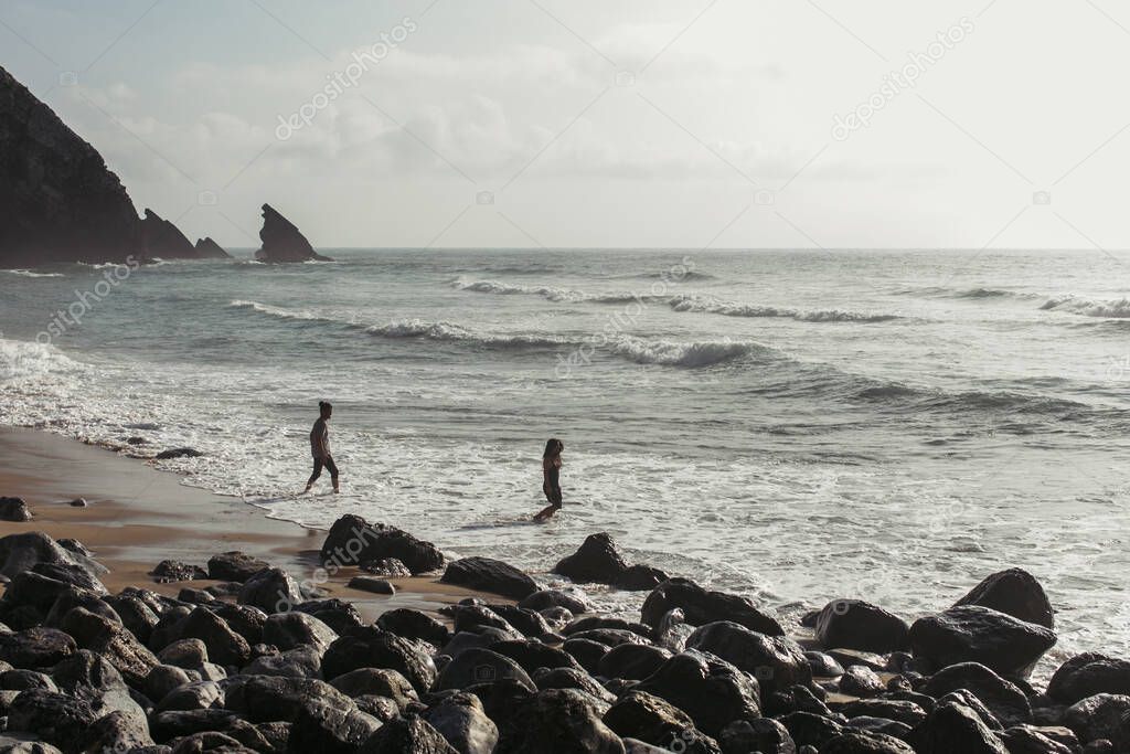 happy bearded man looking at girlfriend in dress walking into ocean water 