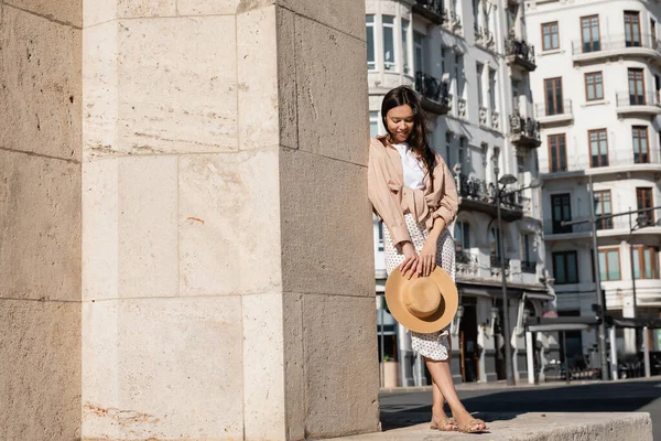 Volle Länge der stilvollen Frau mit Strohhut in der Nähe der Mauer auf der städtischen Straße — Stockfoto