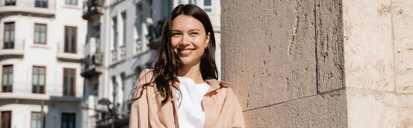 Happy brunette woman smiling on city street near wall, banner — Photo de stock