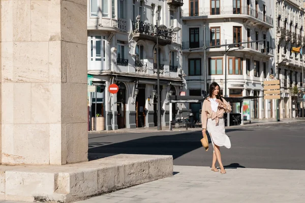 Full length of brunette woman in skirt walking along urban street - foto de stock