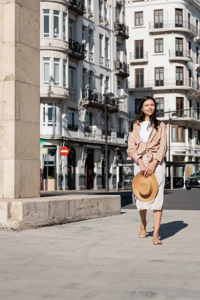 In voller Länge Ansicht der brünetten Frau mit Strohhut zu Fuß auf der Straße der Stadt — Stockfoto