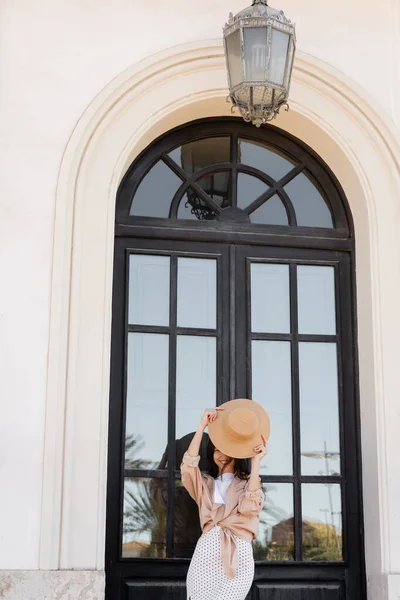 Cheerful woman obscuring face with straw hat near arch window — Fotografia de Stock