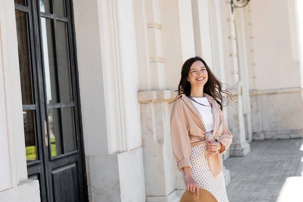 Stylish brunette woman smiling near white building with black door — Photo de stock