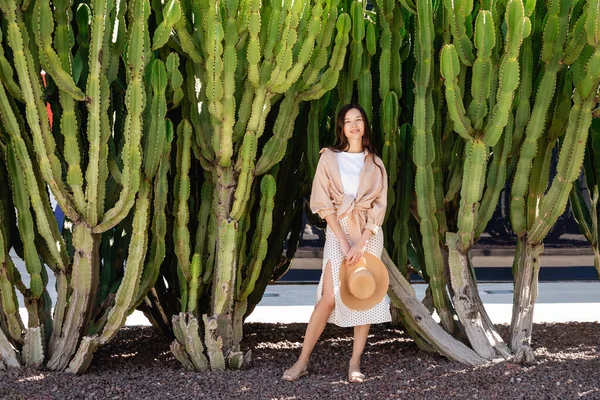 Piena vista lunghezza della donna sorridente in piedi con cappello di paglia vicino cactus enormi — Foto stock