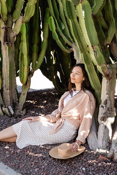 Happy woman in skirt sitting in park near giant succulents — стоковое фото