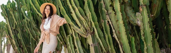 Fröhliche Frau in trendiger Kleidung und Strohhut neben riesigen Kakteen, Banner — Stockfoto