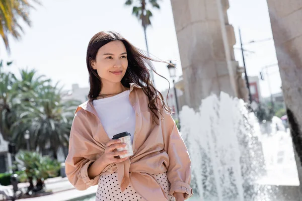 Довольная женщина в бежевой рубашке стоя с кофе, чтобы пойти в город — стоковое фото
