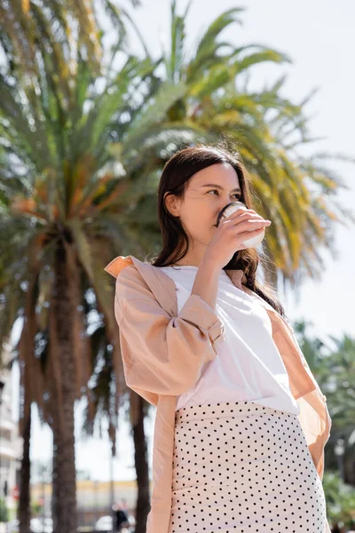 Стильная женщина пьет кофе, чтобы пойти в размытый парк — стоковое фото
