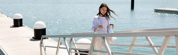 Brunette woman with takeaway drink walking on sea pier, banner — Stock Photo
