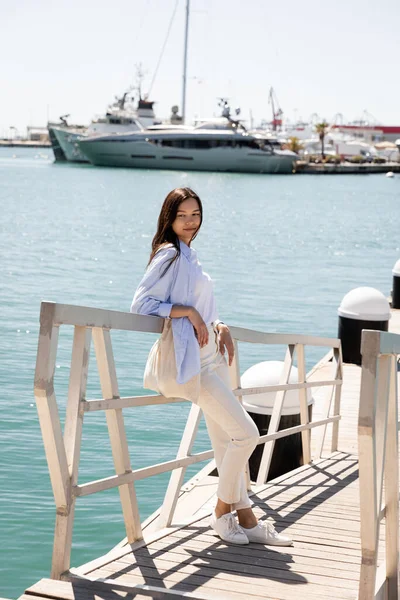 Ganzkörperansicht einer Frau in weißen Hosen, die auf einem Steg im Seehafen steht — Stockfoto