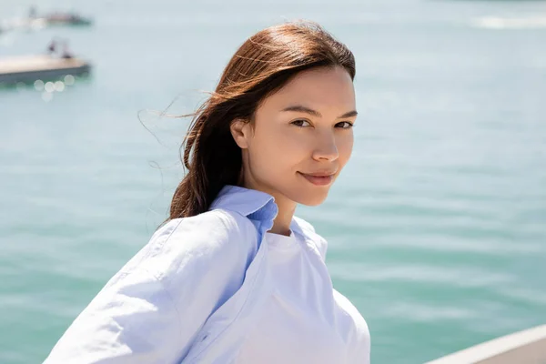 Portrait of positive brunette woman looking at camera near sea — стоковое фото