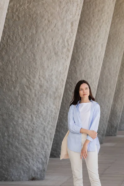 Brunette woman in blue shirt looking away near grey wall — стоковое фото