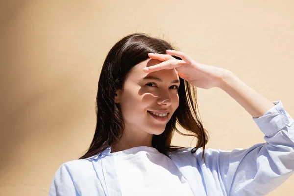 Cheerful brunette woman holding hand above eyes and looking away outdoors — Stock Photo