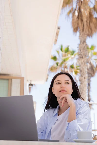 Thoughtful woman looking away near laptop and coffee cup on cafe terrace — Stockfoto